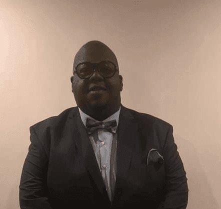 Person wearing a suit with a bow tie, standing against a plain background.